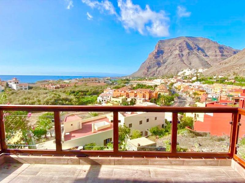 View from a terrace with glass railing over a village, mountains, and the sea.