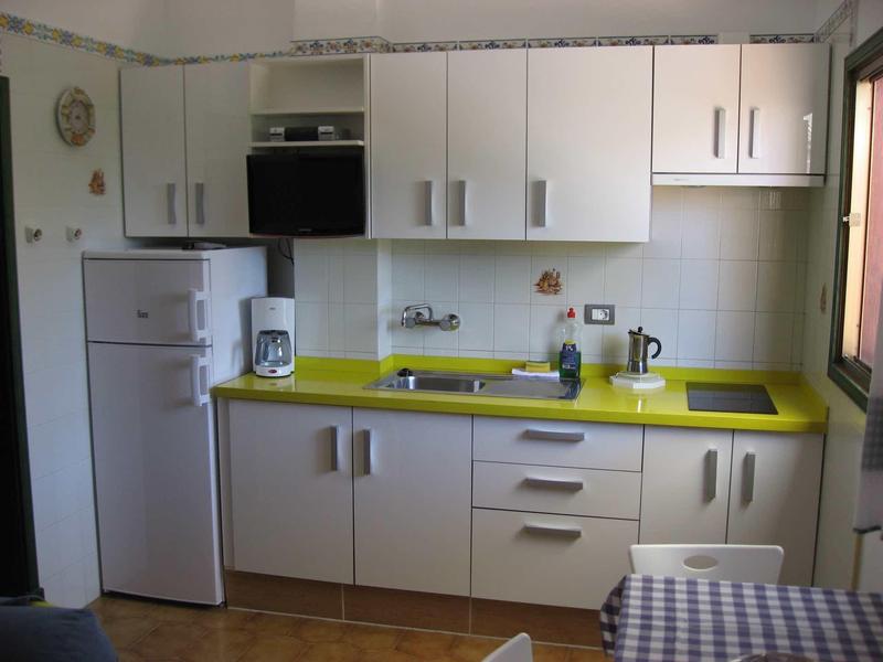Small kitchen with white cabinets and yellow countertop, fridge and coffee maker.