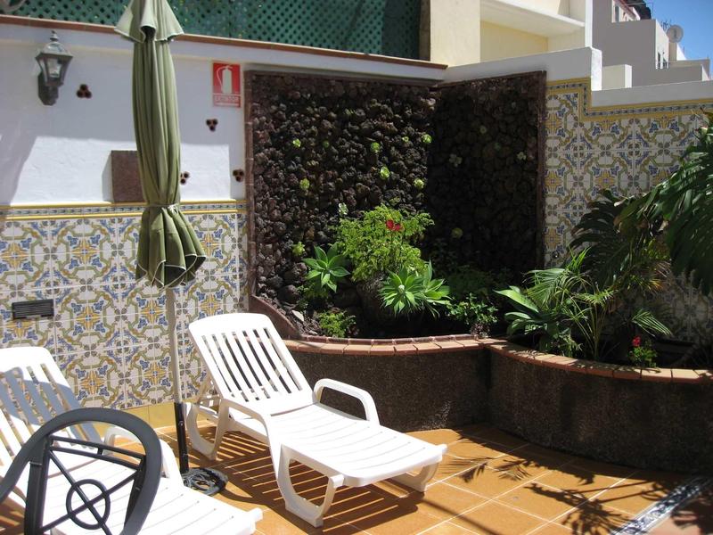 Sun lounger on a terrace with plants and decorative tile pattern on the wall.