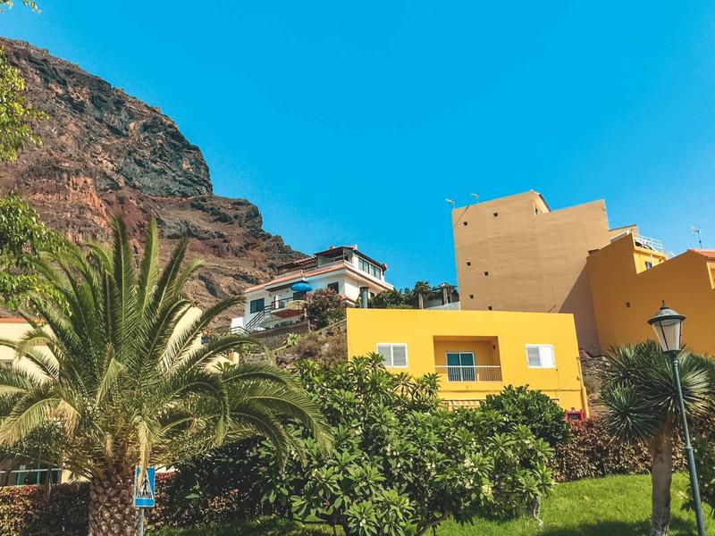Yellow building with rocky mountain backdrop and palm trees under clear blue sky.