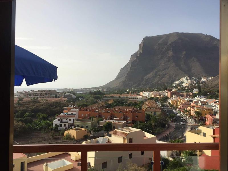 View of a coastal town with mountain backdrop, houses, and a blue sunshade