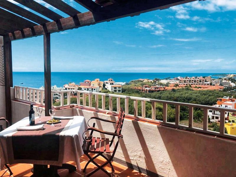 Balcony with set table and chairs overlooking the sea and blue sky.