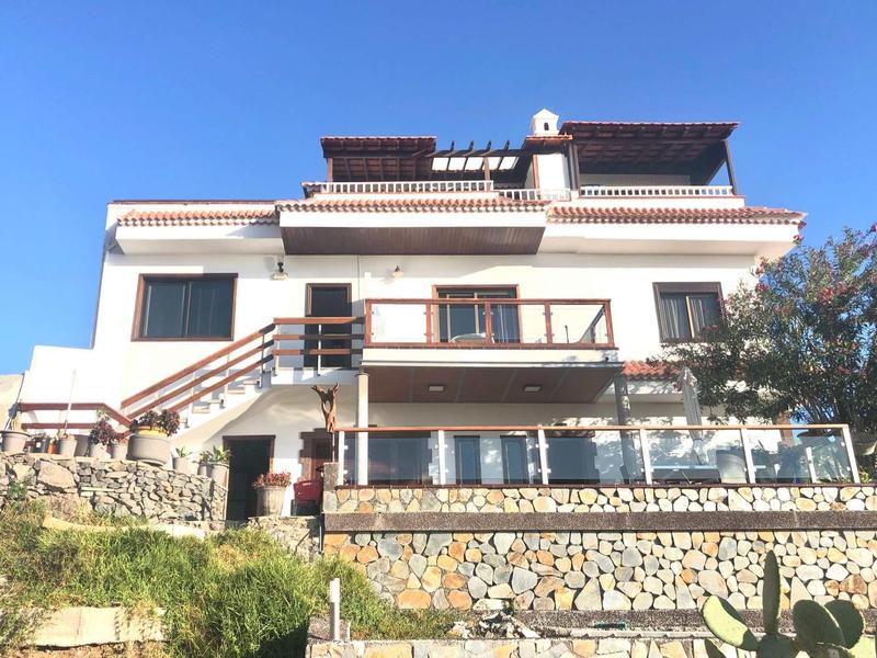 Large white building with multiple balconies and stone foundation under a blue sky.