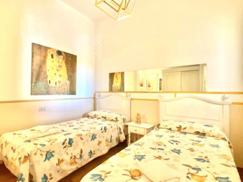 Bright bedroom with two single beds and floral bedding, a mirror, and light decor.