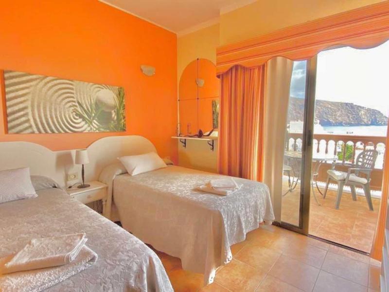 Hotel room with two single beds, orange wall, and balcony with mountain view.