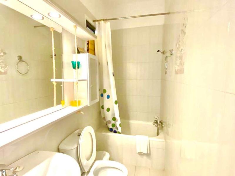 Small bathroom with toilet, sink, bathtub, and shower curtain in a bright space.