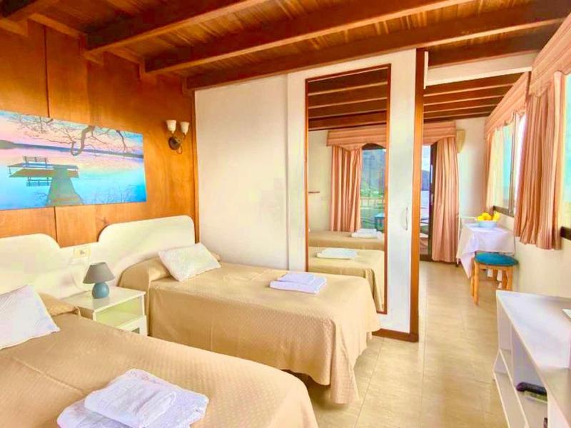 Bright hotel room with two single beds, mirrored wardrobe, and sea view through windows.