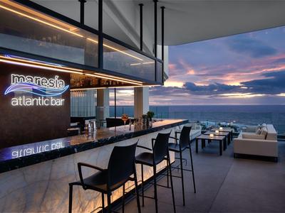 Moderní bar s pultem a sezením s výhledem na moře při západu slunce.