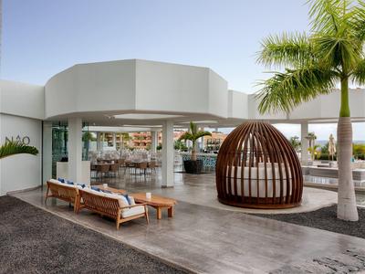 Moderní venkovní prostor hotelu s lehátky a dřevěným pavilonem pod palmami.