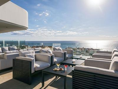 Moderní terasa s pohodlnými křesly a výhledem na moře za slunečného dne.