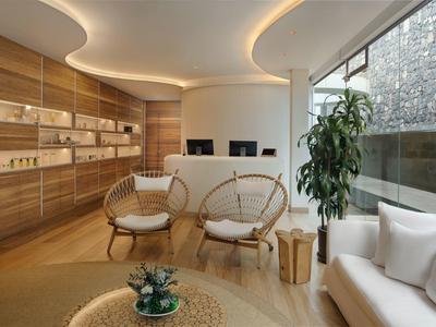 Moderně zařízená hotelová lobby s proutěnými křesly, pohovkou a velkými okny.