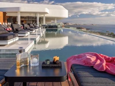 Moderní nekonečný bazén na terase s výhledem na moře a pohodlnými lehátky.