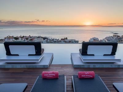 Zwei Liegen mit Polstern auf einer Terrasse mit Meerblick bei Sonnenuntergang.