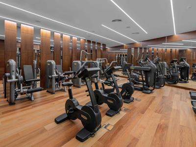 Modern gym with wooden flooring and rows of cardio and strength machines.