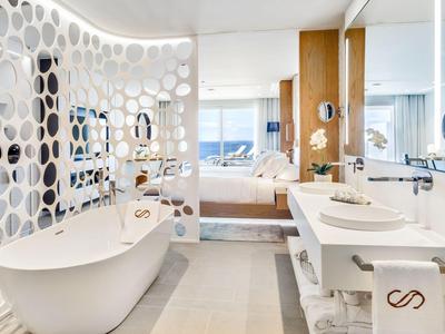 Modern bathroom with freestanding tub and perforated circular divider in bright hotel room.