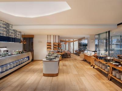Modern hotel lobby with buffet area, wooden flooring, and bright lighting.