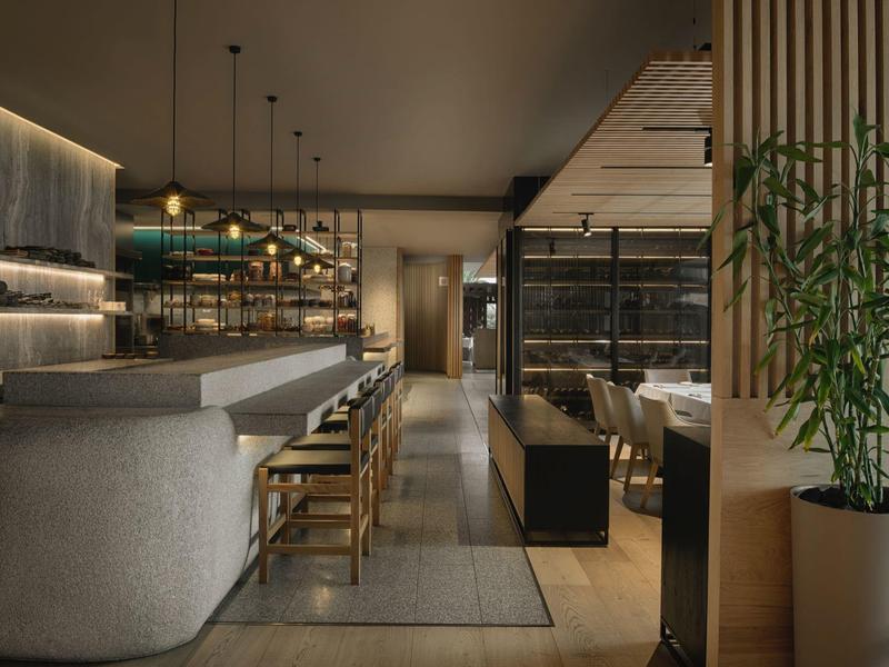 Moderní hotelový bar s dřevěnými židlemi, tlumeným osvětlením a elegantním designem.