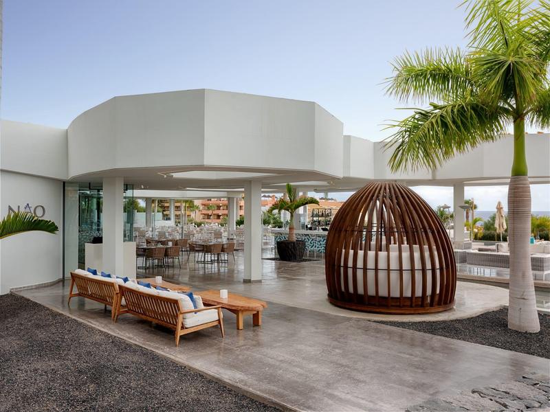 Moderní venkovní prostor hotelu s lehátky a dřevěným pavilonem pod palmami.