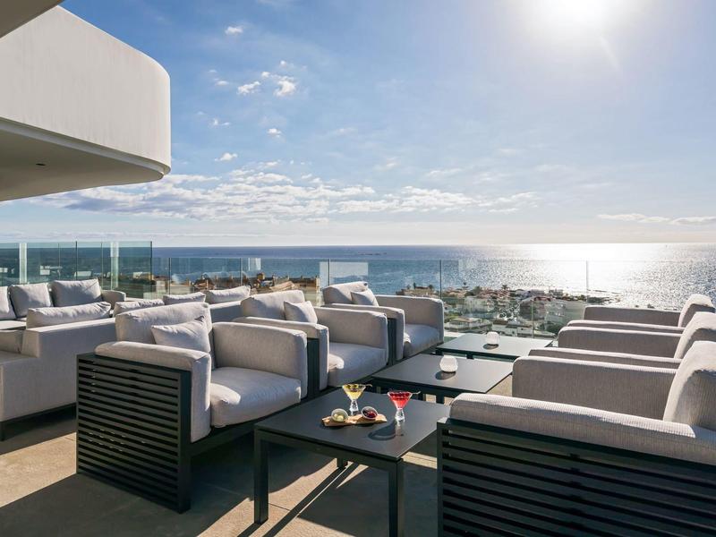 Moderní terasa s pohodlnými křesly a výhledem na moře za slunečného dne.