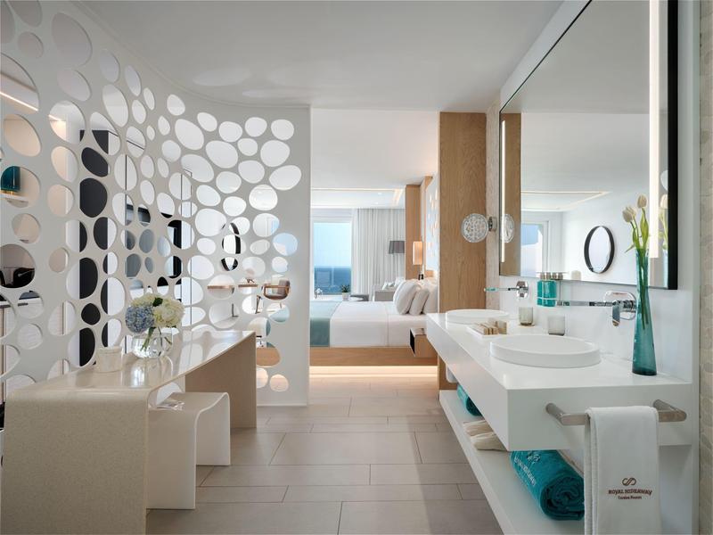 Moderní hotelová koupelna s velkým zrcadlem, bílými umyvadly a dekorativní příčkou.