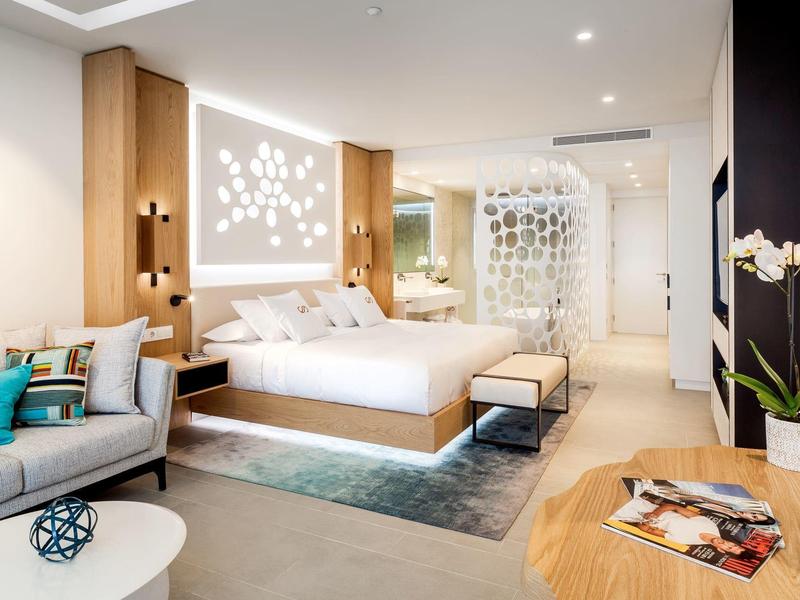 Moderní hotelový pokoj s manželskou postelí, posezením a elegantním designem v světlých barvách.