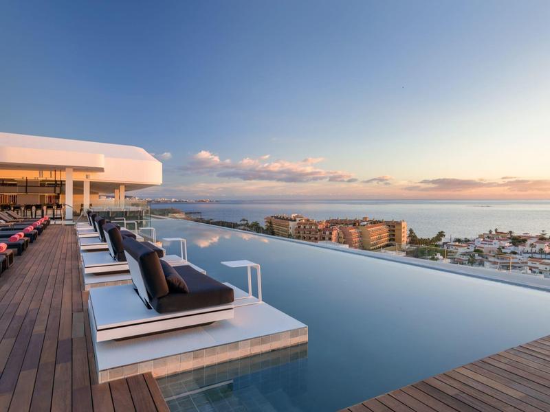 Nekonečný bazén na terase s výhledem na město a moře při západu slunce.