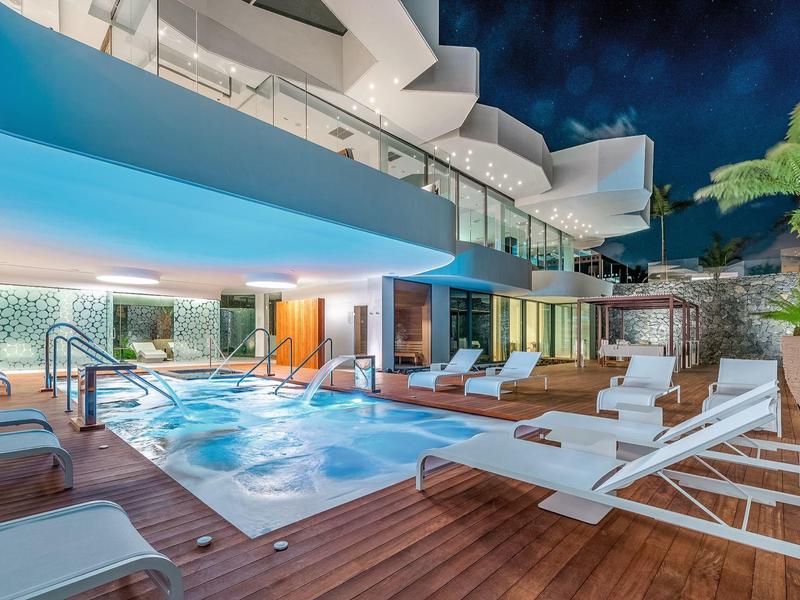 Moderní venkovní bazén s lehátky a osvětlením v hotelu v noci.