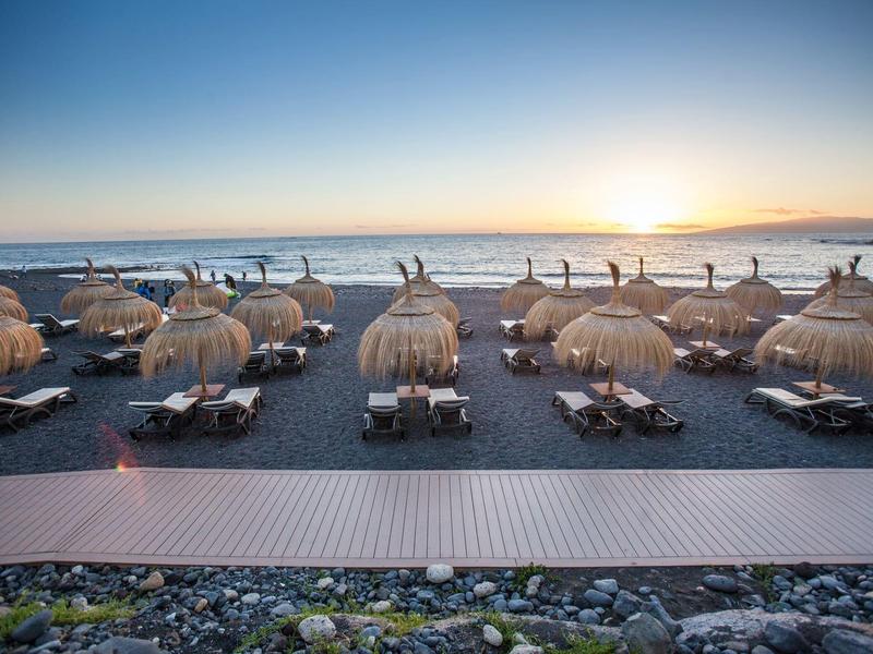 Pláž s rákosovými slunečníky a lehátky při západu slunce u moře