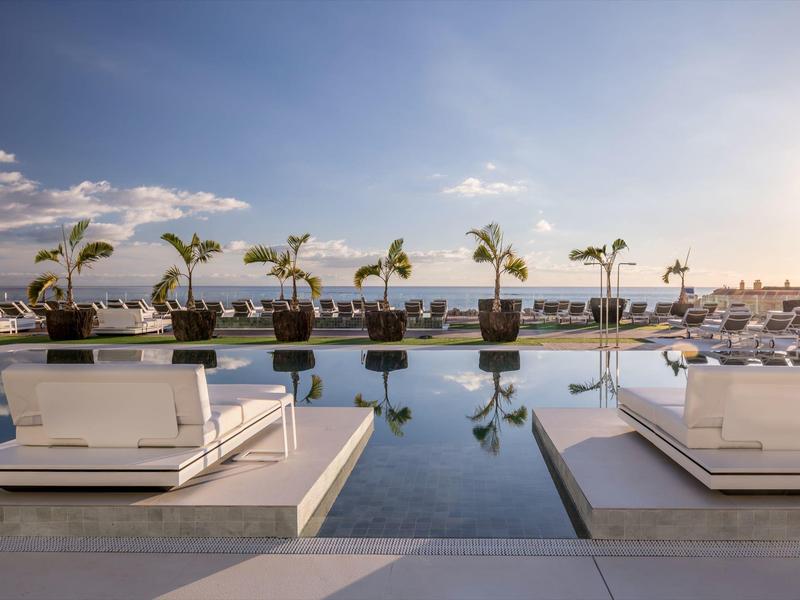 Modern pool area with loungers and palm trees under blue sky at hotel