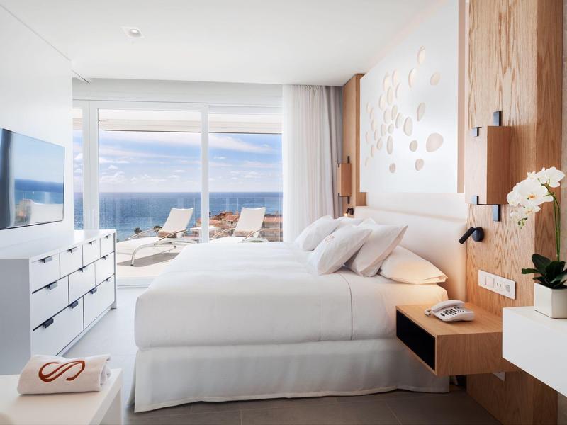 Modern bedroom with large bed and sea view through glass wall