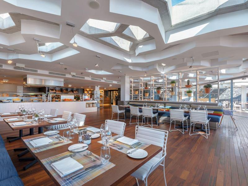 Modern restaurant with wooden floor, white furniture, and distinctive ceiling with skylights