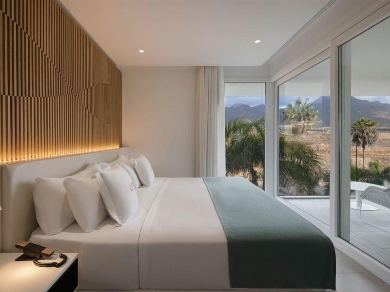 Modern hotel room with large bed and panoramic windows overlooking mountains.