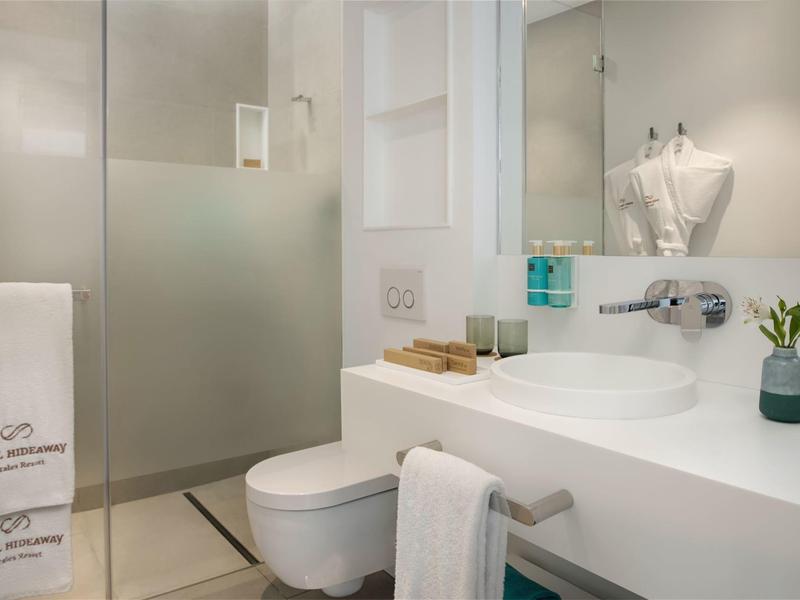 Modern white bathroom with toilet, sink, mirror, and frosted glass shower partition.