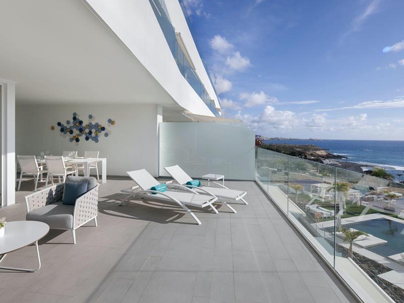 Large terrace with white lounge chairs and glass railing overlooking the sea.