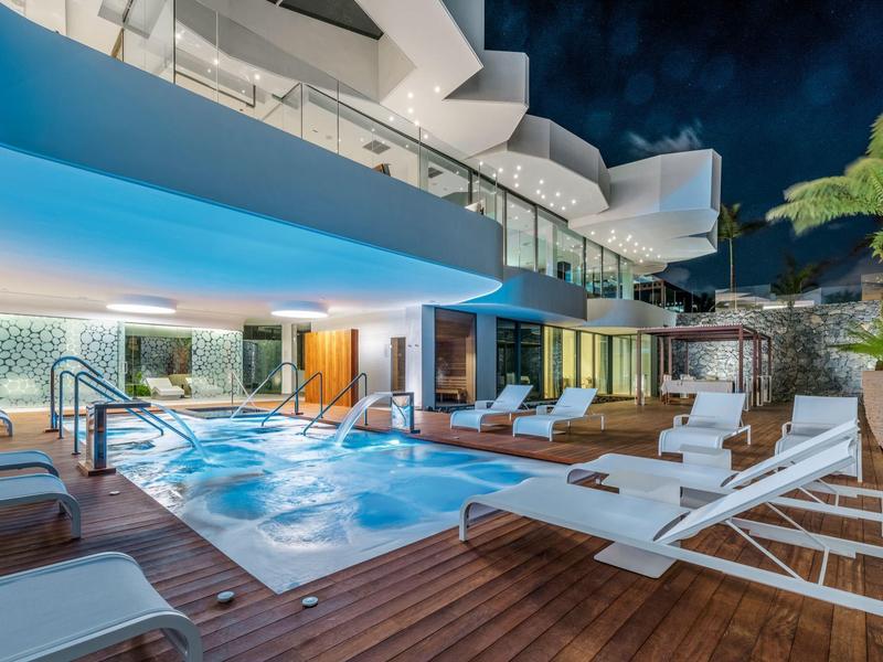 Modern outdoor pool area with lounge chairs and wooden flooring at a hotel.