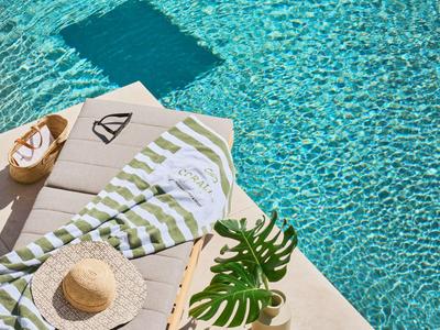 Liegestuhl mit Handtuch, Hut und Pflanze neben klarem Poolwasser mit schwimmendem Tablett.