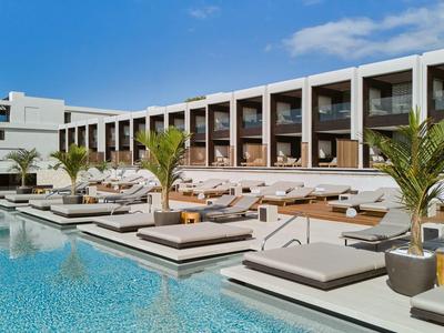 Nowoczesny hotelowy basen z leżakami i palmami pod niebieskim niebem.