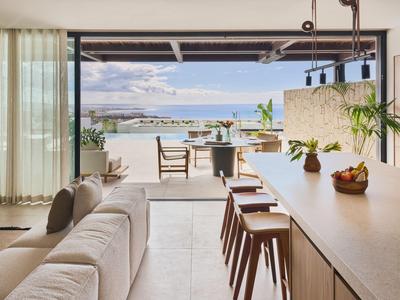 Moderne offene Wohnküche mit Blick auf Terrasse und Meer bei klarem Himmel.