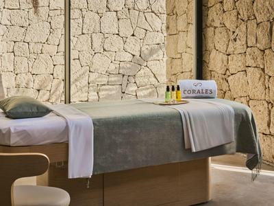 Stół do zabiegów na tle kamiennej ściany z ręcznikami i produktami do pielęgnacji w spa.