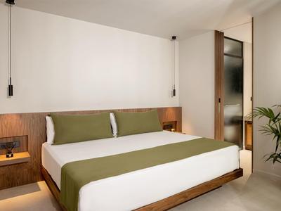 Nowoczesny pokój hotelowy z podwójnym łóżkiem, drewnianymi meblami, zielonymi akcentami i roślinami.