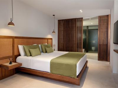 Nowoczesny pokój hotelowy z dużym łóżkiem, zielonymi akcentami i drewnianymi meblami.