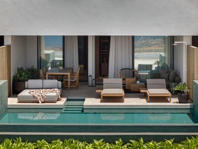 Nowoczesny teren zewnętrzny z basenem, dwoma leżakami, sofą i stołem przed szklaną elewacją.