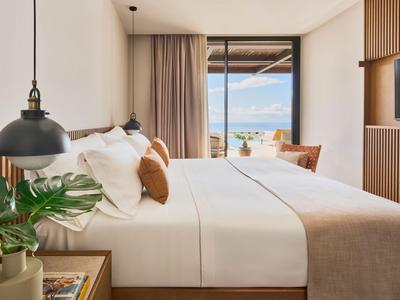 Schlafzimmer mit Doppelbett, braunen Vorhängen und Meerblick durch große Fenster.