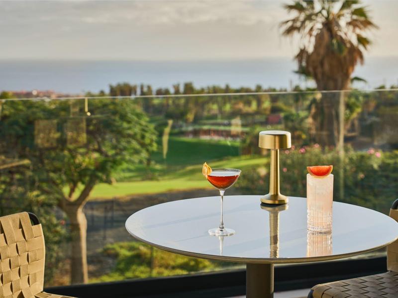 Nowoczesny stół na zewnątrz z napojami i świecą z widokiem na zielony ogród i palmy.