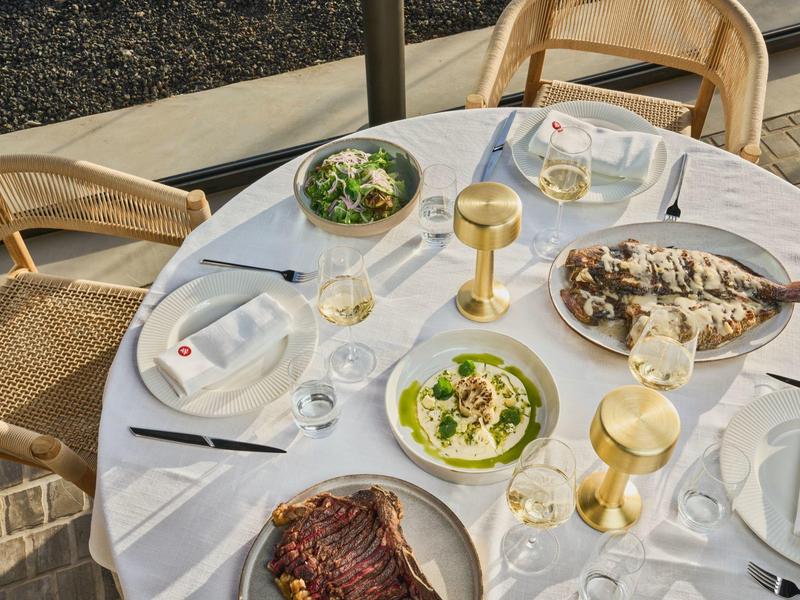 Okrągły stół z białym obrusem, dania rybne i napoje w złotych kieliszkach.