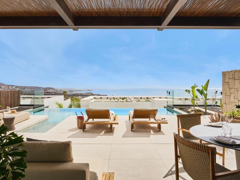 Luksusowy taras z basenem, leżakami i widokiem na morze przy czystym niebie.