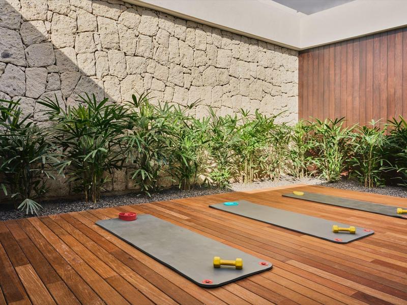 Strefa relaksu z matami do jogi na drewnianej podłodze i roślinami przy kamiennej ścianie w hotelu