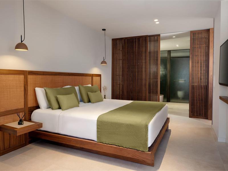 Nowoczesny pokój hotelowy z dużym łóżkiem, zielonymi akcentami i drewnianymi meblami.