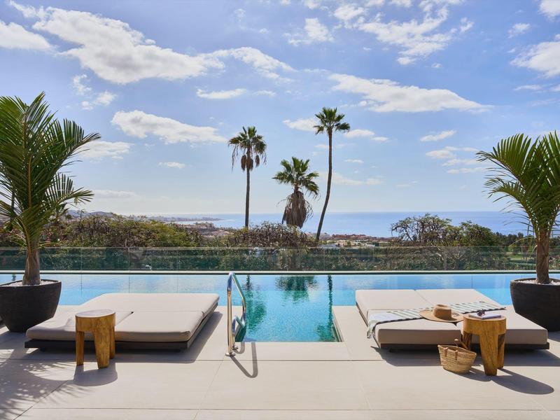 Nowoczesny basen z leżakami, palmami i widokiem na morze pod czystym niebem.