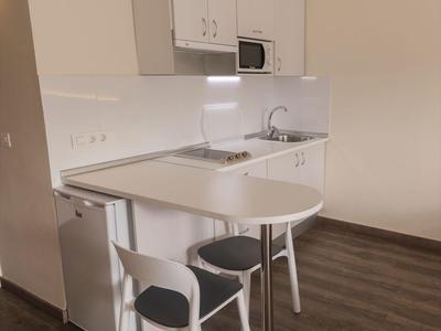 Piccola angolo cottura bianca con bancone, due sgabelli e pavimento in legno in una stanza.